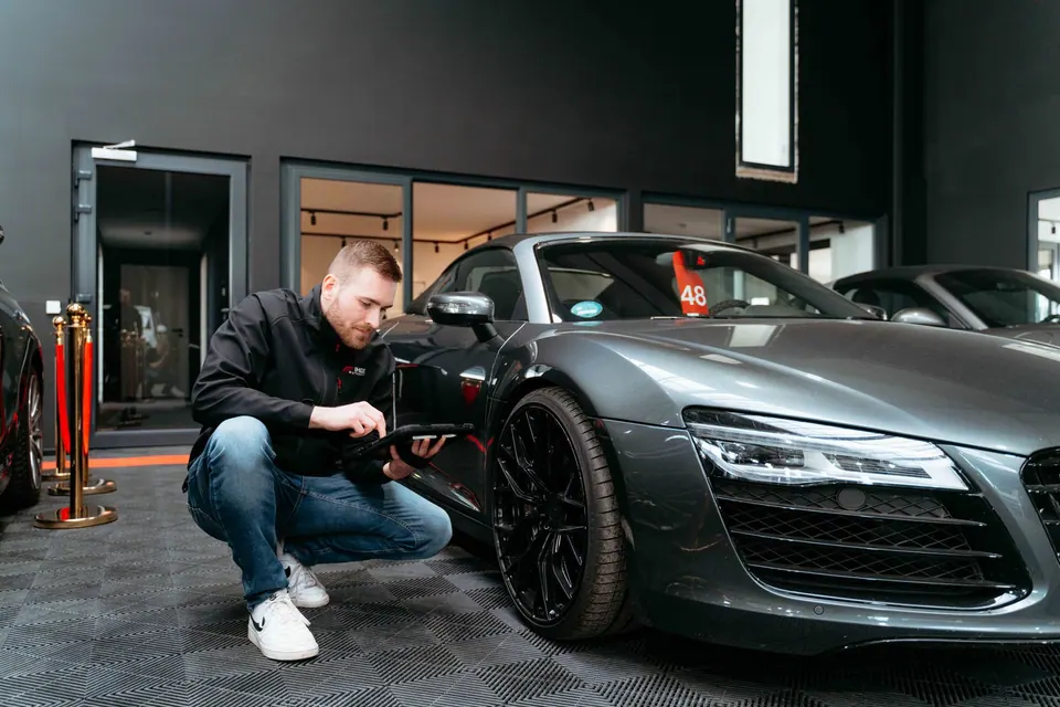Kfz-Sachverständiger inspiziert schwarzes Audi-Fahrzeug in moderner Werkstatt mit Tablet