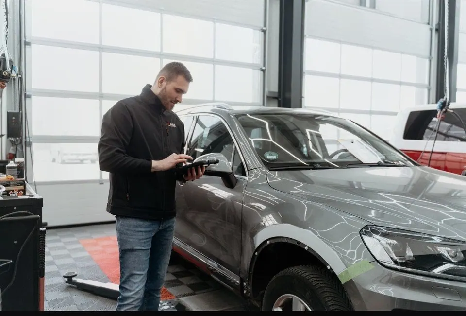 Techniker inspiziert graues Auto mit Tablet